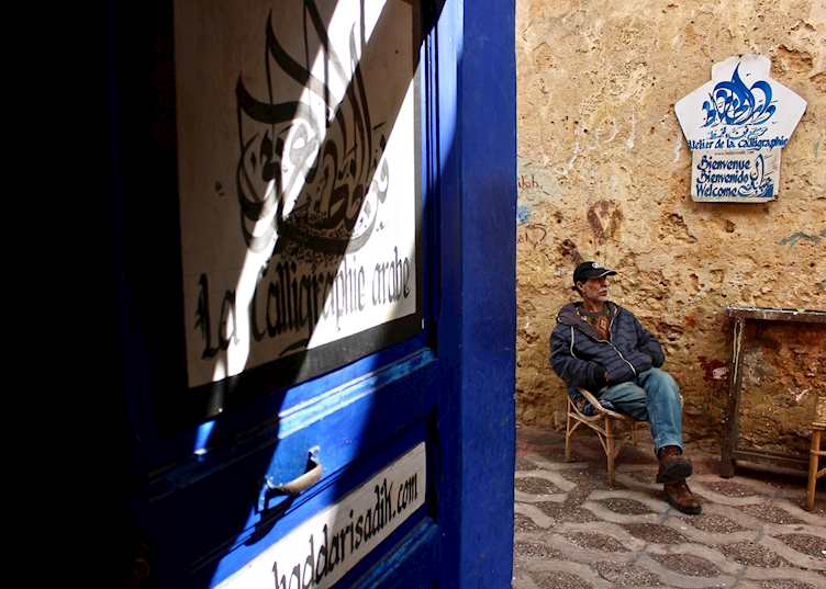 A man sits outside of Asilah's Arabic calligraphy shop