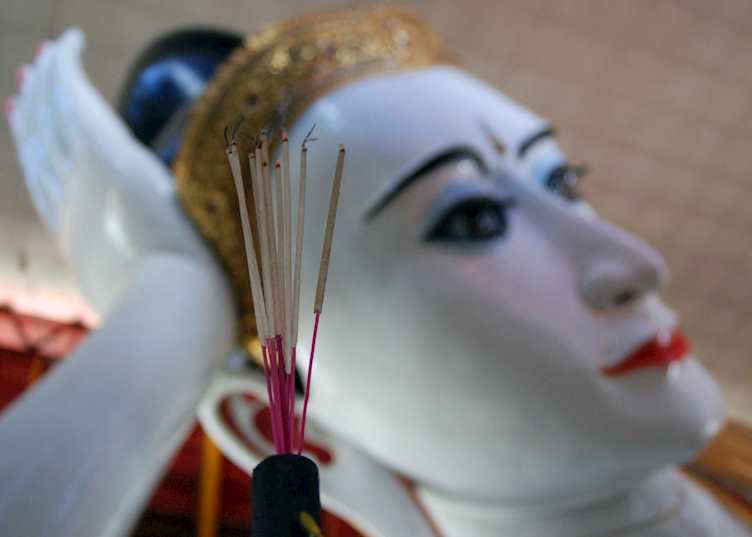 Incense sticks burn below the enormous reclining Buddha in Yangon
