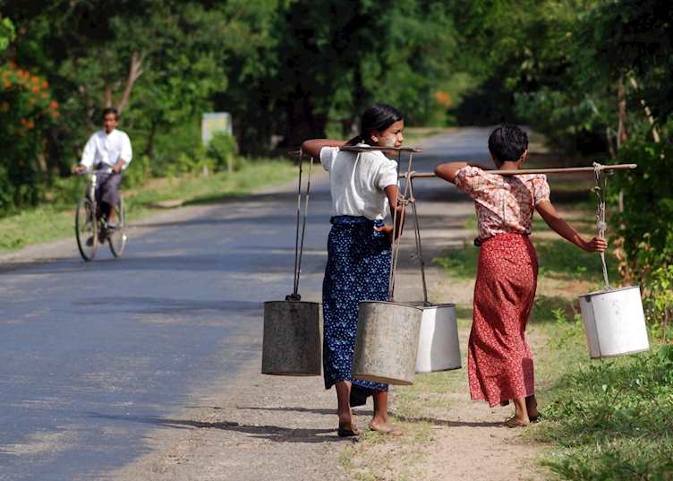 Young ladies carrying water walk the road to Mount Popa