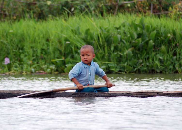 A young Burmese boy paddles on the home-made boat, Inle Lake